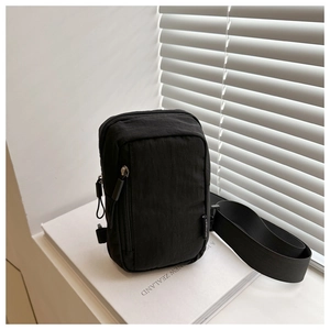 Detail shot of black nylon crossbody bag with vertical zipper on white books