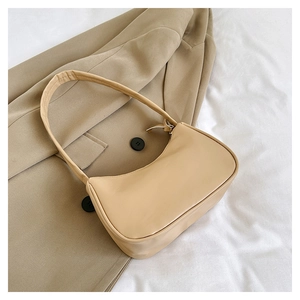 Detailed close-up of beige minimalist underarm bag on soft white fabric with blazer
