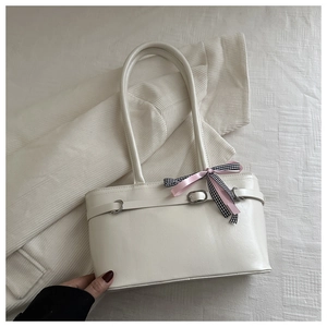 Détail d'un sac à main crème orné d'un ruban à carreaux rose dans un décor cocooning