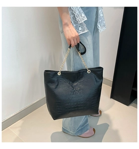 Detail of black faux crocodile leather tote bag with gold chain strap held by a model