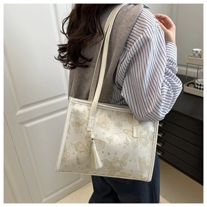 Detailed view of white tote bag featuring golden butterfly prints and a matching tassel