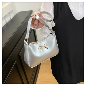 Detail of silver metallic handbag with a gold bow accent worn with a white shirt