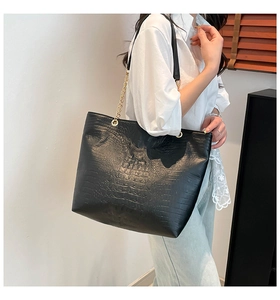 Detail of black crocodile embossed tote bag with gold chain strap on model's shoulder