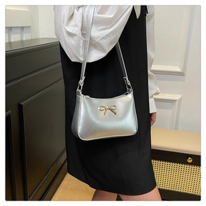 Close-up of metallic silver shoulder bag featuring a decorative gold bow hardware detail
