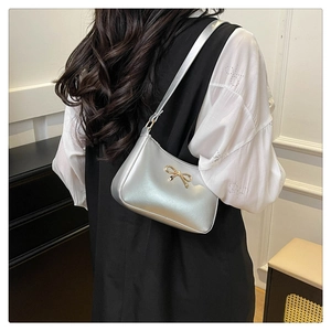 Detail of silver shoulder bag with metallic finish and gold 3D bow metal accessory