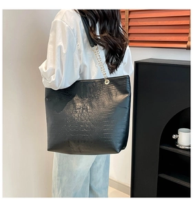 Close-up of black crocodile pattern tote bag with gold chain strap on female model