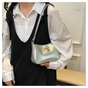 Detail of silver shoulder bag with a gold bow buckle on white shirt and black dress