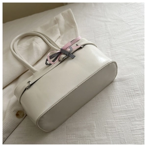 Détail d'un sac à bandoulière crème chic avec un nœud à carreaux rose sur tissu blanc
