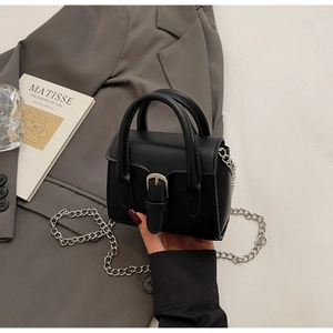 Détail d'un mini sac à main noir avec boucle argentée et chaîne sur une veste grise