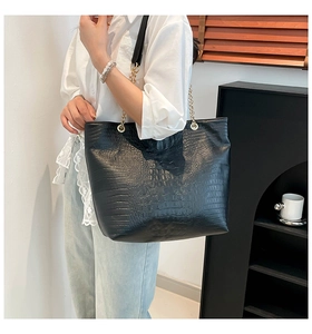 Detail of black crocodile texture tote bag with gold metal chain strap on shoulder