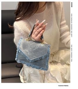 Close-up of blue denim mini bag featuring fringe edges and gold chain strap detail