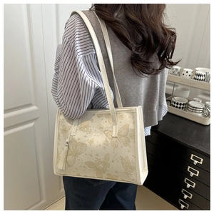 Detail of off-white tote bag featuring golden butterfly print and elegant side tassel