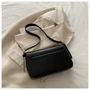 Detail of a black leather crossbody bag with gold hardware on a beige blazer