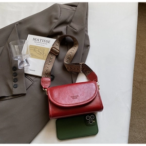 Detail of burgundy vintage crossbody bag with wide jacquard strap on grey blazer jacket