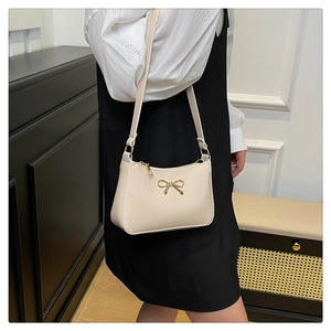 Detail of a chic cream shoulder bag featuring a gold metal bow and zipper closure