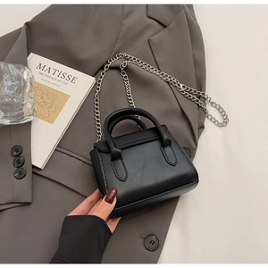 Petit sac carré noir chic posé sur un blazer gris avec bandoulière chaîne argent