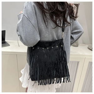 Vista dettagliata della borsa a secchiello nera con frange e anelli dorati su outfit casual