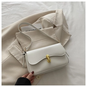 Close-up of a cream white flap bag with gold U-shaped metal clasp on a beige blazer