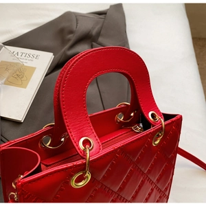 Detail of red quilted patent leather handbag with gold hardware on a grey suit background