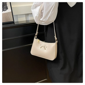 Detail of a beige PU leather shoulder bag featuring a decorative metal bow and slim strap