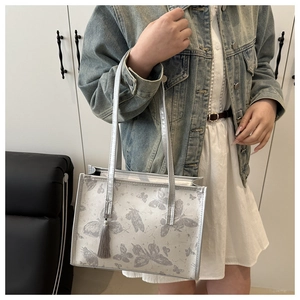 Close-up of silver tote bag with butterfly prints, tassel charm and metallic finish