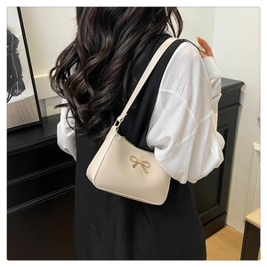 Detail of a chic shoulder bag featuring a delicate gold bow metal clasp on smooth PU leather
