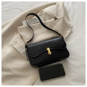 Detail of black matte leather shoulder bag with gold U-shaped buckle on a beige blazer