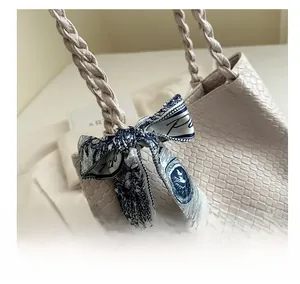 Close-up of beige woven tote bag details with artistic blue patterned silk scarf handle