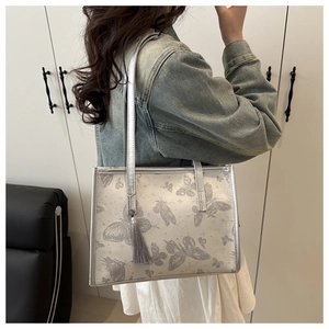 Detail of silver tote bag with butterfly prints and elegant fringe pendant