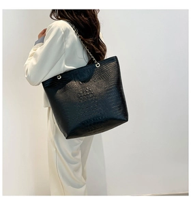 Detail of black tote bag with faux crocodile pattern and gold metal chain strap detail