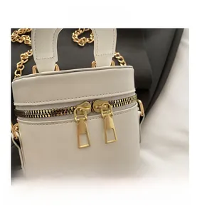 Gros plan du sac seau en cuir grainé blanc avec double fermeture éclair dorée et chaîne
