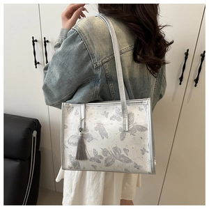 Detail of silver tote bag with butterfly patterns and grey tassel on a model shoulder