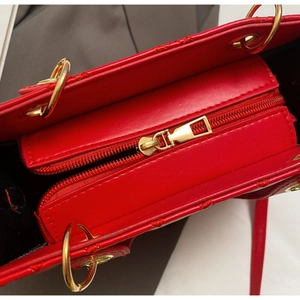 Close-up of red quilted leather bag showing gold zipper and metal handle ring detail