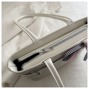 Détail de la fermeture éclair argentée et du ruban sur le sac cabas en cuir blanc crème