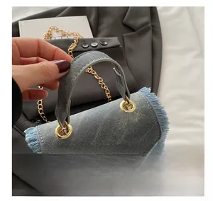 Detail view of light blue denim handbag featuring retro fringe edges and gold chain strap