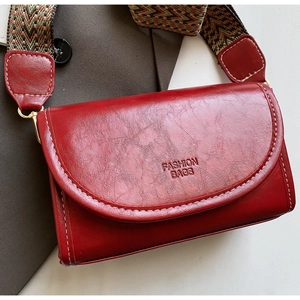 Detail of red vintage leather square bag with fashion logo and ethnic woven strap