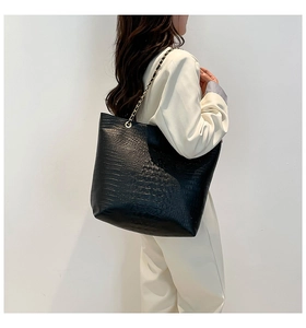 Detail view of black crocodile pattern tote bag with gold chain strap on model shoulder