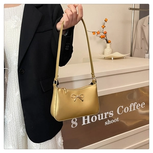 Detail of a chic golden shoulder bag featuring a metallic bow and smooth leather texture