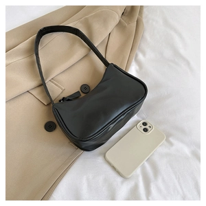 Close-up of minimalist black underarm bag next to phone for size reference and scale
