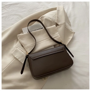 Detail of a dark brown faux leather shoulder bag with gold hardware on a beige blazer