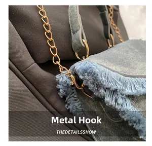 Detail of vintage gold metal hook and fringe edge on blue denim crossbody bag