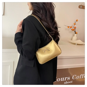 Golden PU leather underarm bag with metal bow clasp shown on a model in a cafe setting