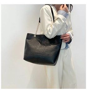 Detail of black crocodile-embossed tote bag featuring a gold chain strap for women