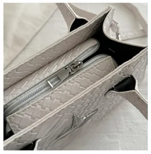 Detailed close-up of smooth silver zipper and white woven texture on leather handbag