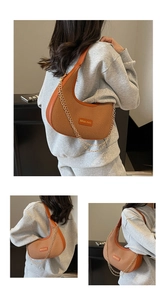 Detail of woven crescent shoulder bag with brown leather trim and gold chain accents