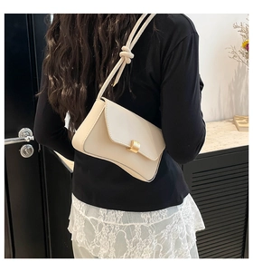 Detail of cream baguette bag featuring metal buckle and knotted strap on model