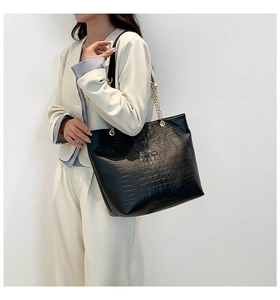 Detail of black faux crocodile leather tote bag with elegant gold chain strap