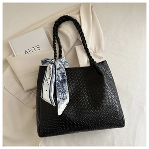 Detail of black woven leather tote bag featuring an elegant floral silk scarf on the handle