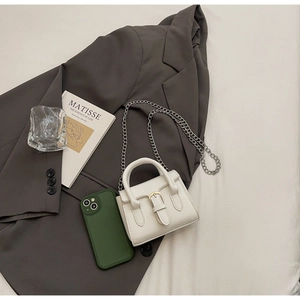 Micro white crossbody bag showing compact size next to a smartphone on a suit background