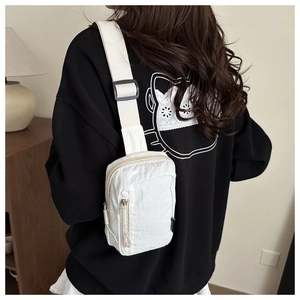 Detailed back view of a white nylon sling bag worn by a model in a minimalist home setting